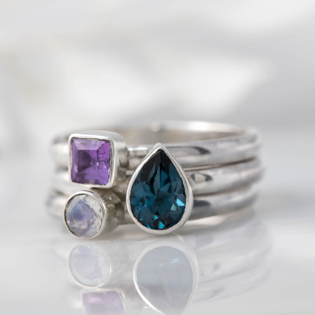 set of three birthstone stacking rings with a london blue topaz pear, amethyst square and round moonstone