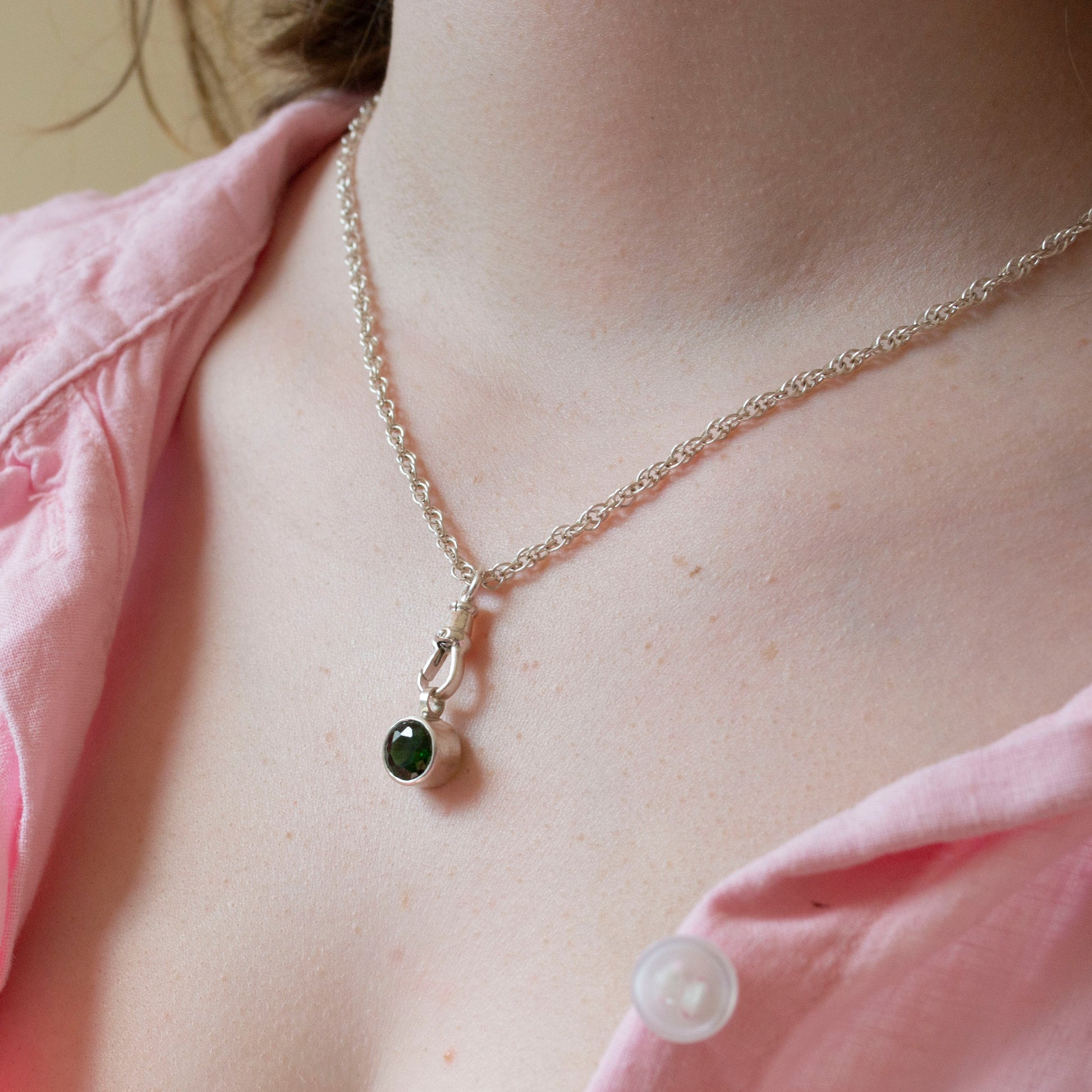 Necklace with a green gemstone pendant worn by a person in a pink shirt.