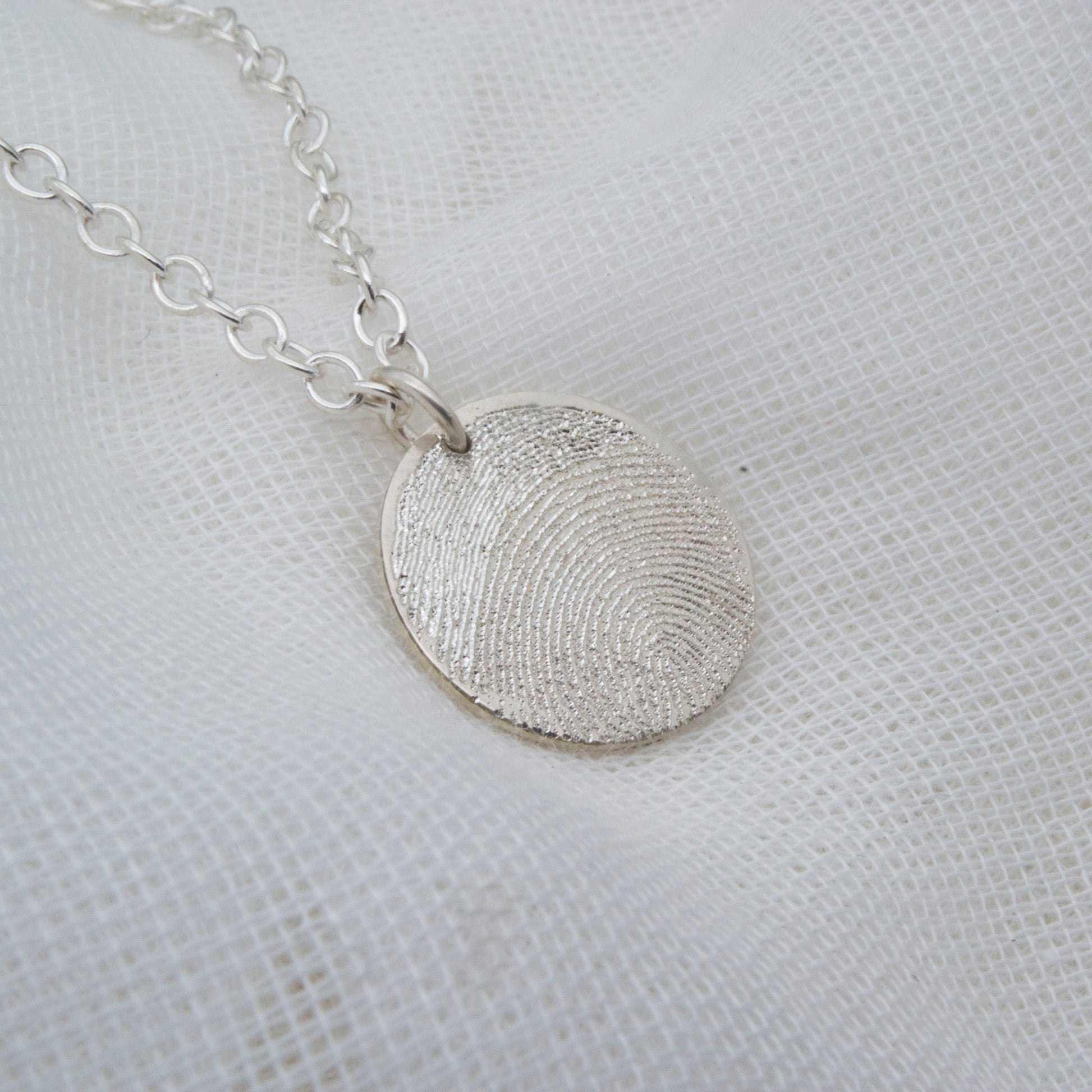 Silver fingerprint necklace on a textured white background